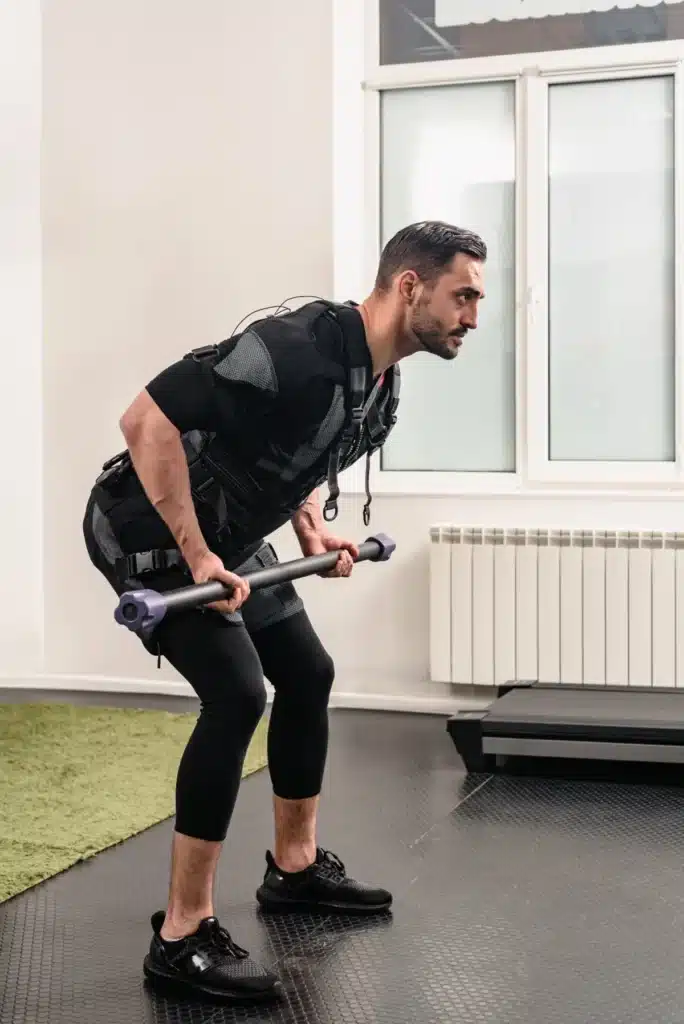 Homme utilisant un dispositif d'électrostimulation tout en réalisant un exercice de barre pour travailler son endurance musculaire. ​​