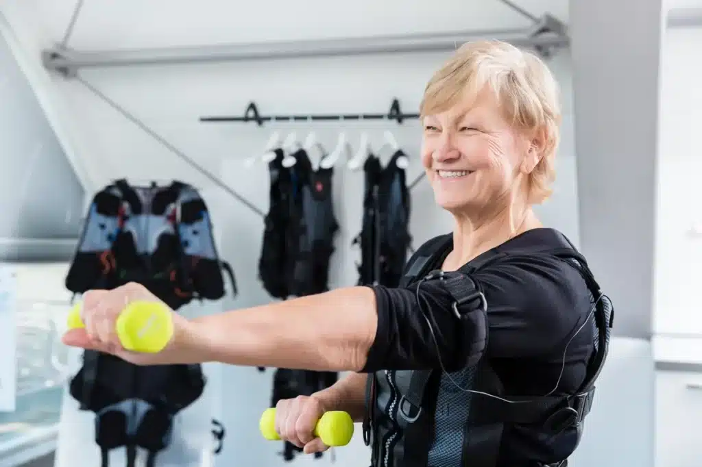 Une femme senior effectuant des exercices d'électrostimulation avec des haltères dans un centre d'amincissement.